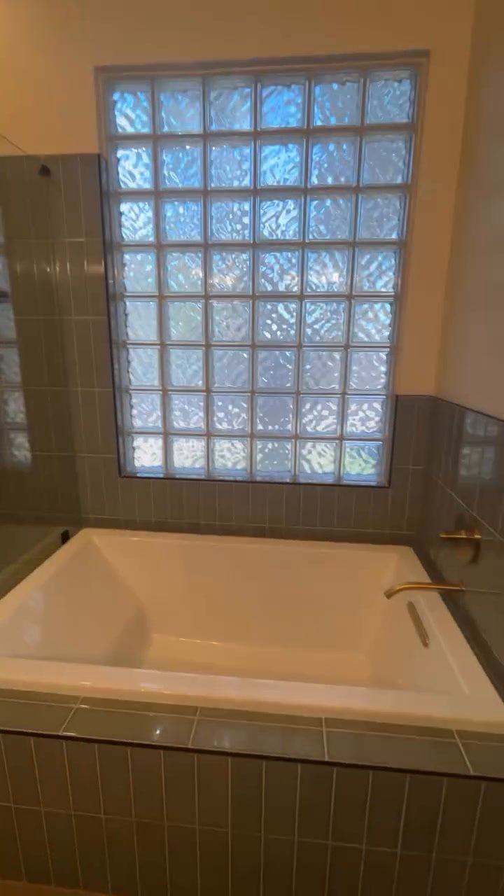 Soaking tub with a tiled deck under the glass block window.