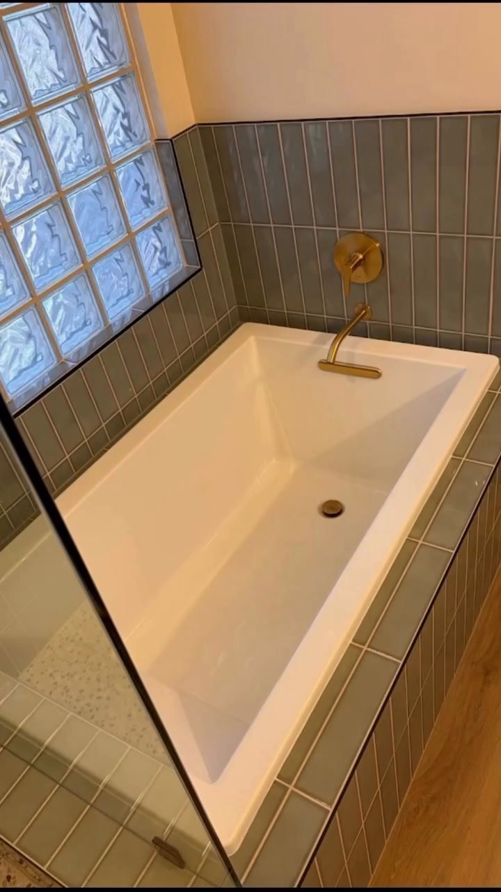 Polished sage green tile wraps the tub deck, finished with a brushed gold wall-mount filler.