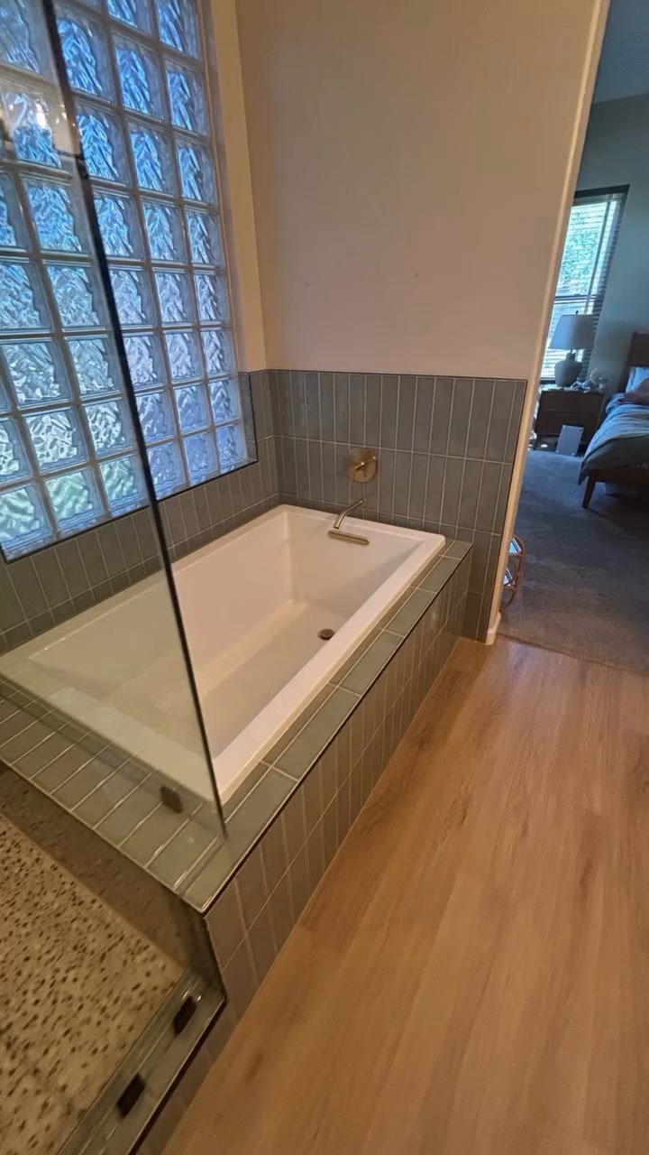 Walk-in shower: vertical sage green tile, pebble floor, built-in niche and brushed gold rain head and handheld.